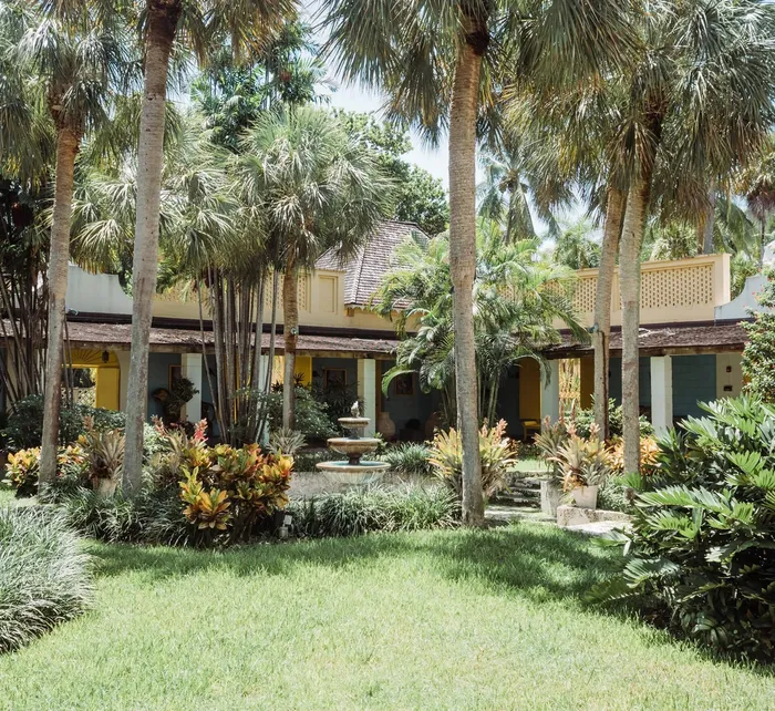 Courtyard at Bonnet House Museum & Gardens with the historic yellow estate, ornate wrought-iron balcony, and decorative gazebo among tropical plants