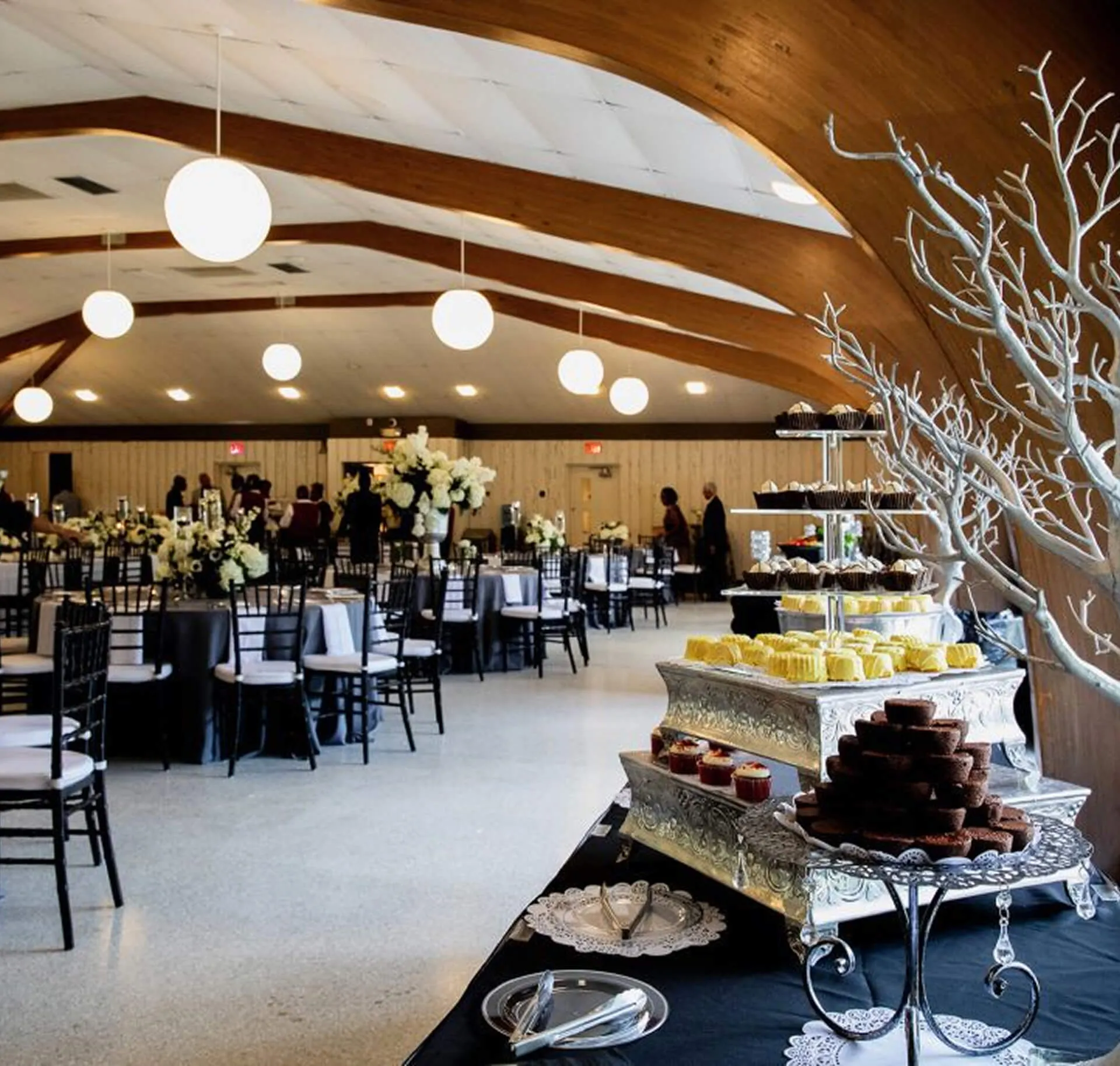 Indoor reception at Venue on Lake Lily in Maitland with dessert display, round dining tables, wood-beam vaulted ceiling, and globe pendant lighting
