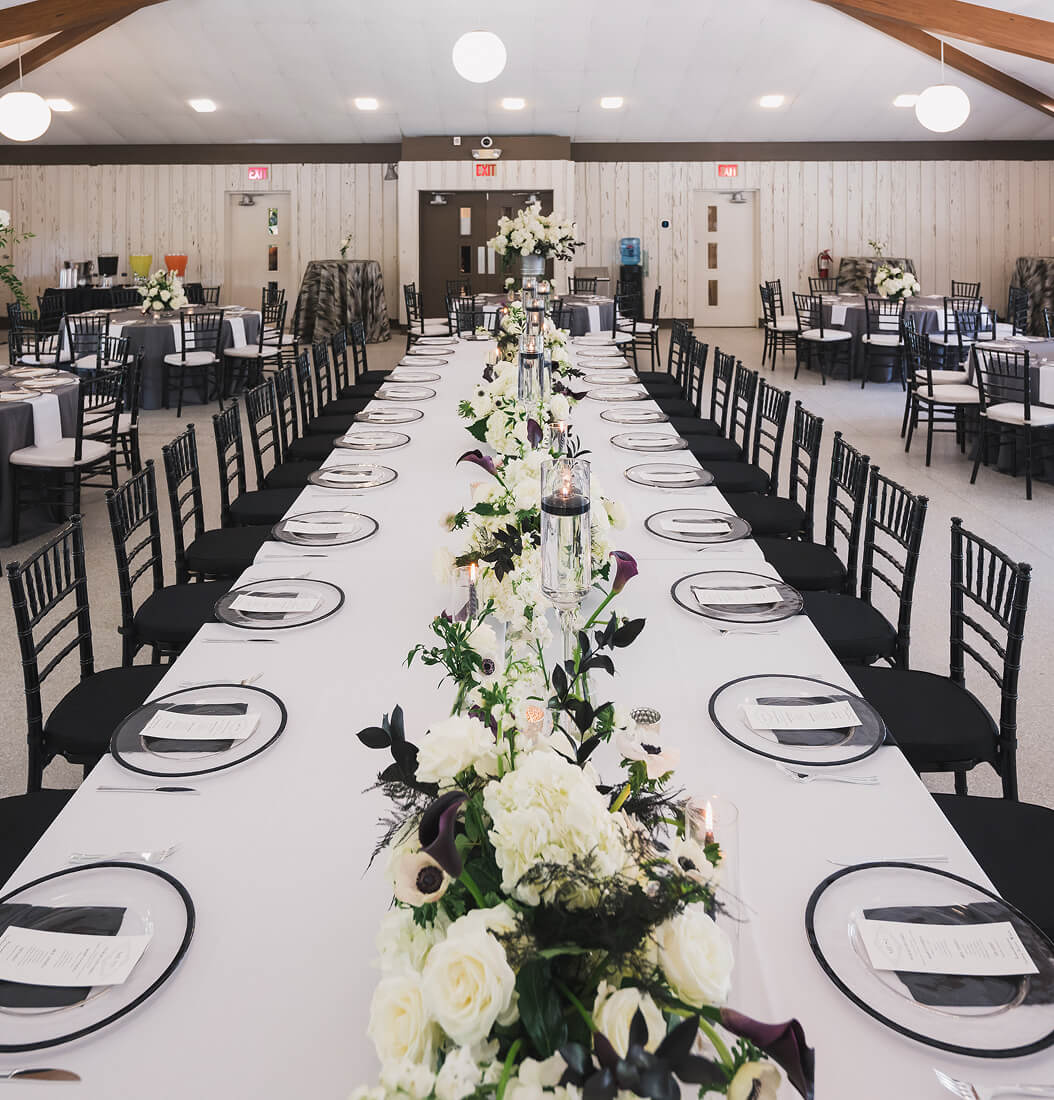 Long head table at Venue on Lake Lily in Maitland with white floral runner, floating candles, and round guest tables in a wood-paneled banquet hall
