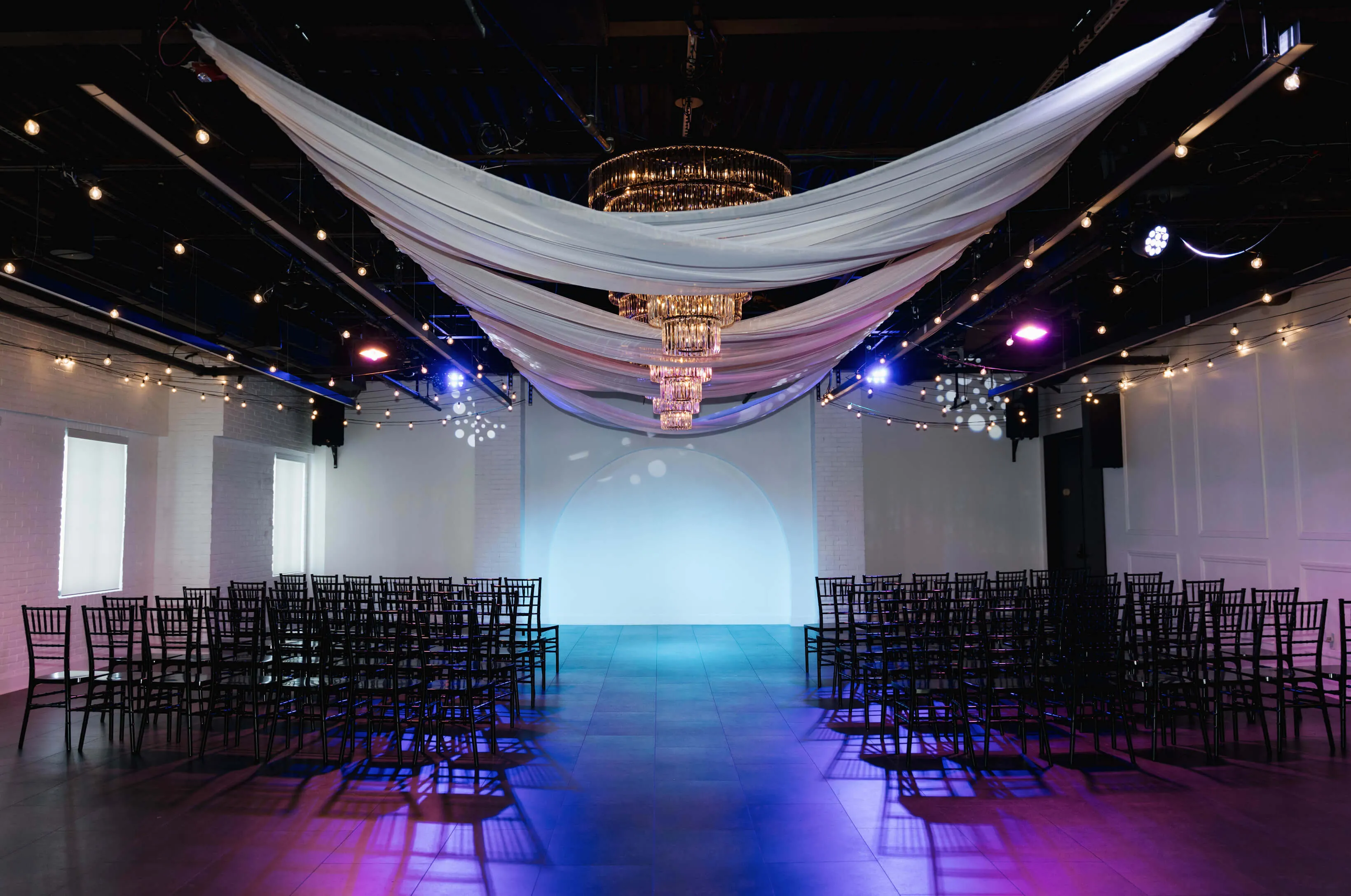 Indoor wedding ceremony setup at Trelis 925 with brick walls, white chairs, and a wooden triangle arch