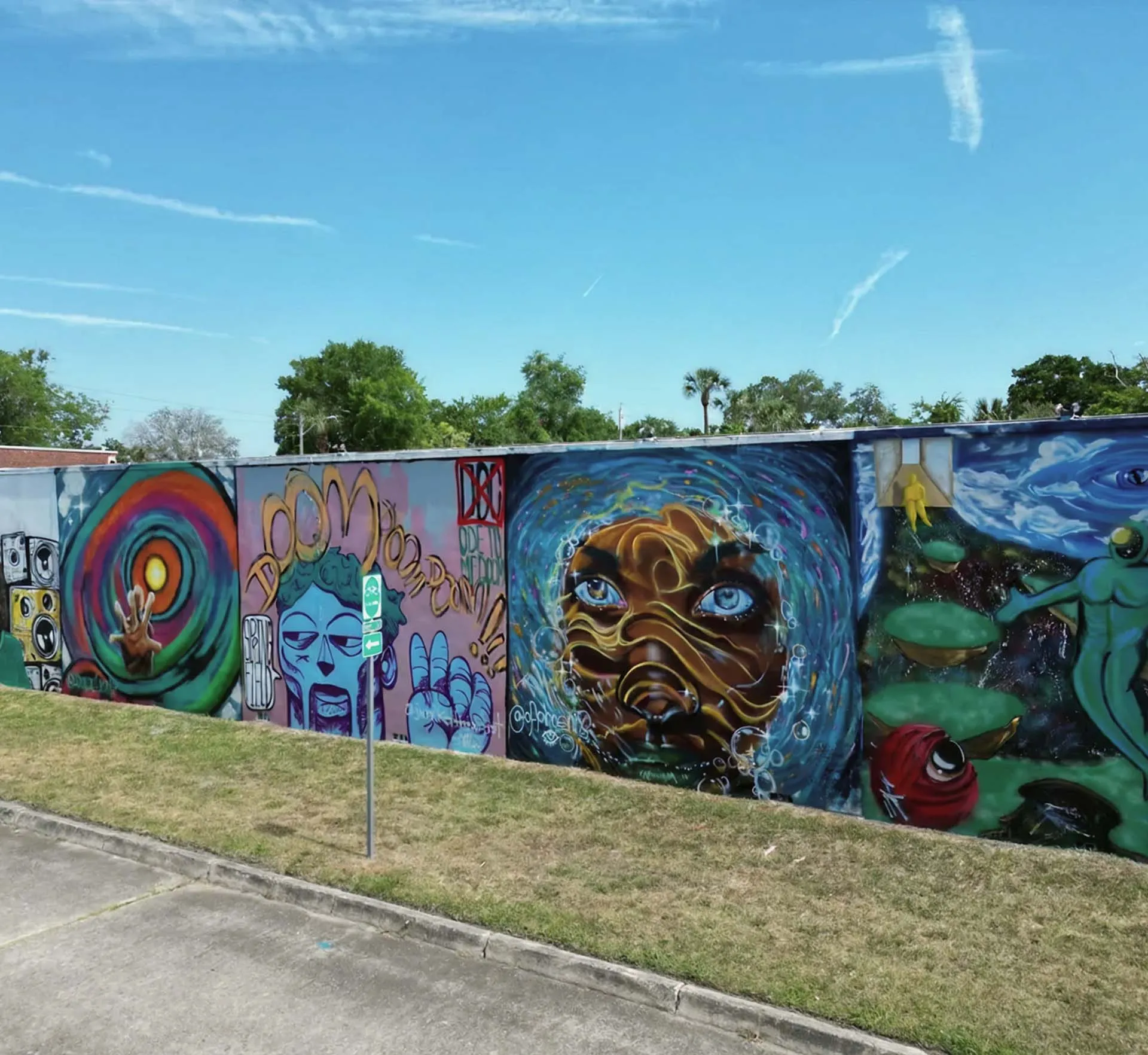 Colorful outdoor mural at The Emerald Station featuring expressive faces, abstract art, and vibrant graffiti under a clear blue sky