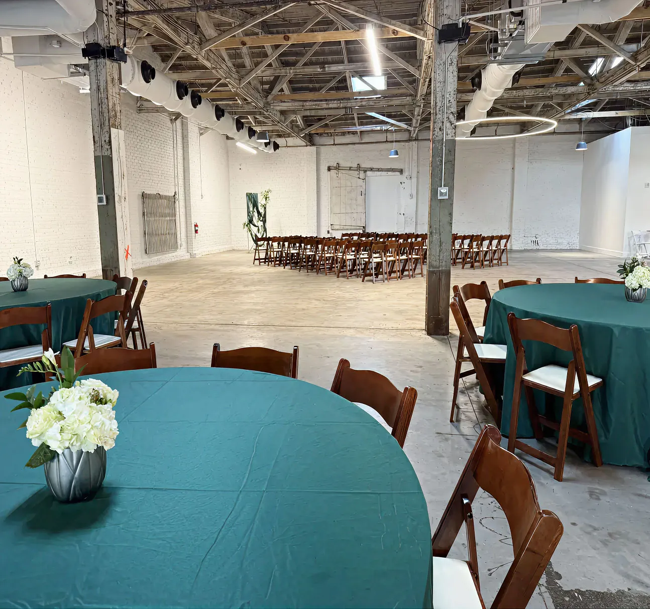 Indoor wedding setup at The Emerald Station with round tables, teal tablecloths, and ceremony chairs in the background
