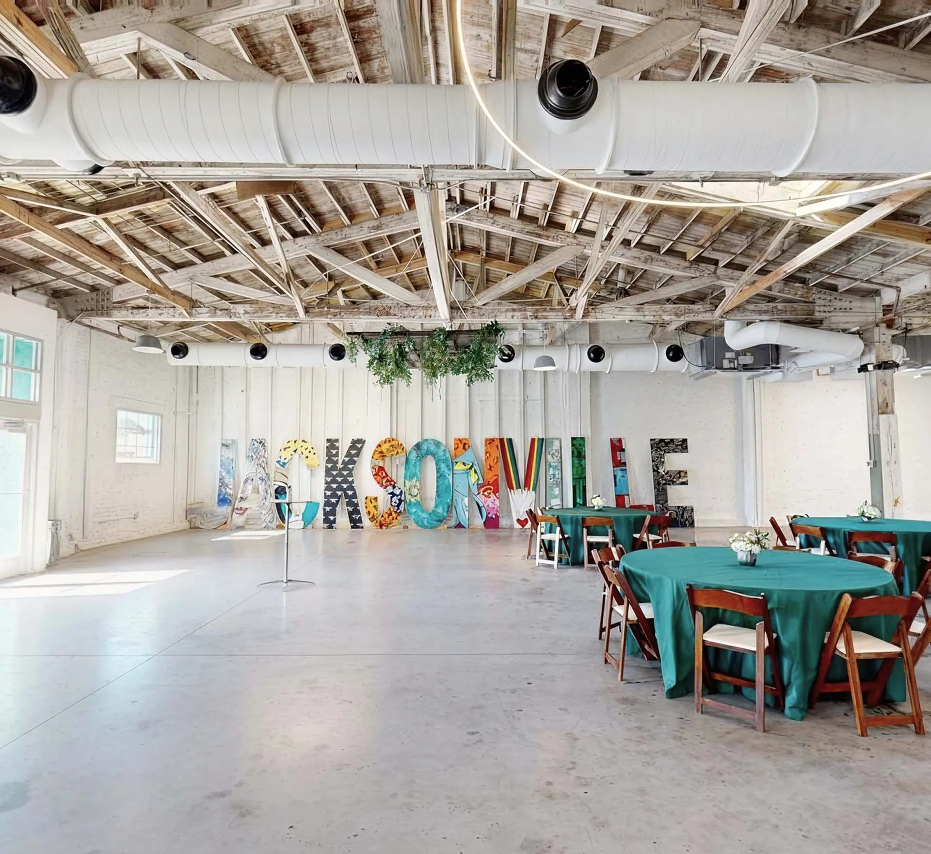 Indoor event space at The Emerald Station featuring rustic wooden ceiling, colorful Jacksonville letters, and round decorated tables