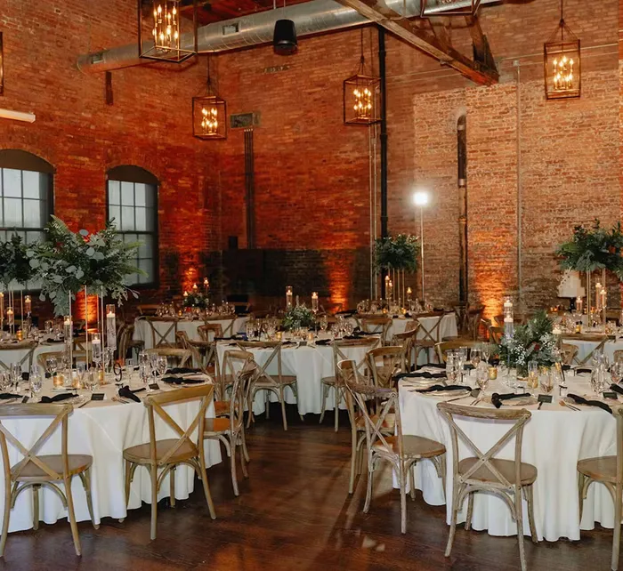 Luxurious indoor wedding reception at Armature Works with tall greenery centerpieces, gold chairs, candlelight, and draped backdrop