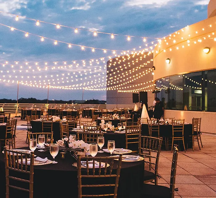Rooftop wedding reception at Orlando Science Center with string lights, round tables, gold chairs, and elegant floral decor overlooking the city