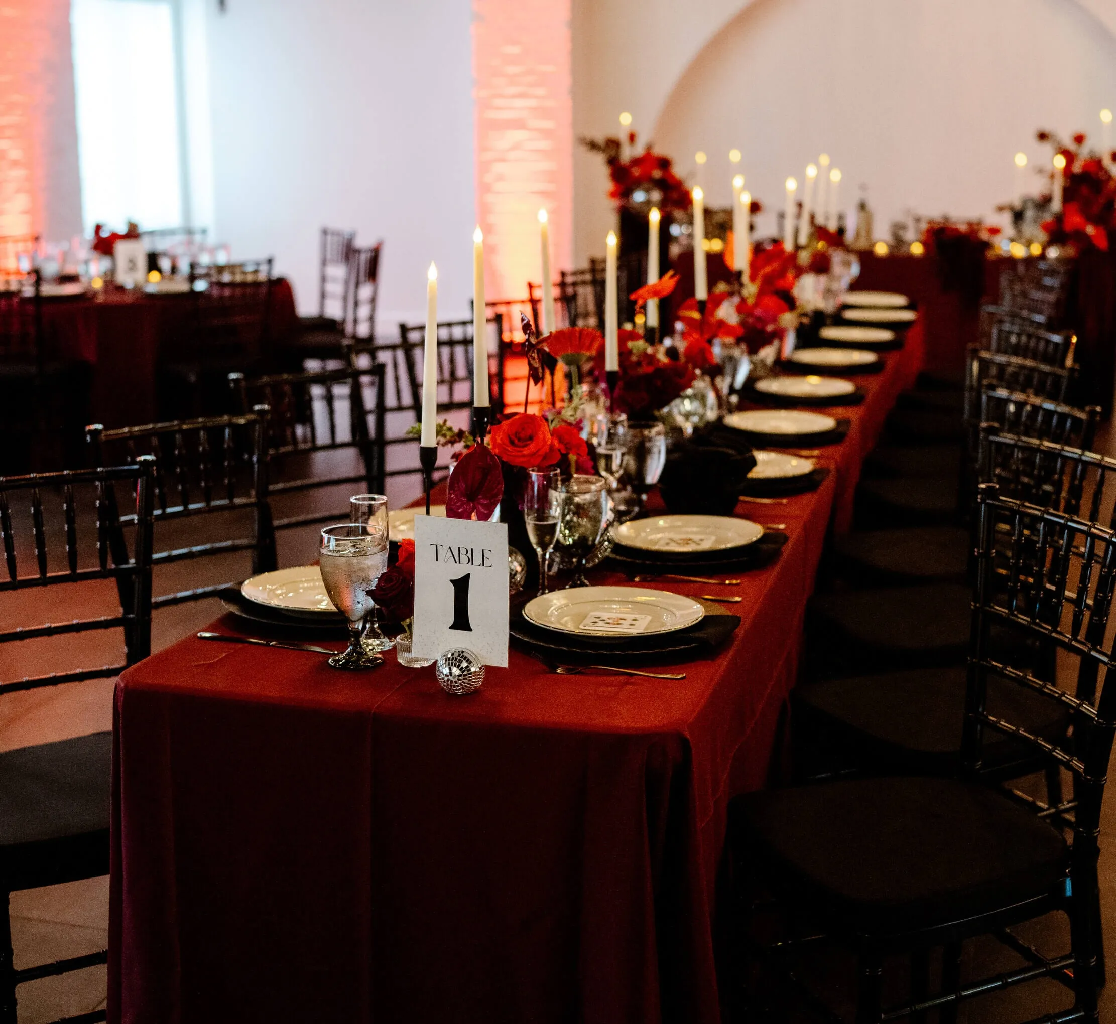 Indoor wedding reception at Trellis 925 with a long table adorned with roses and round tables in the background