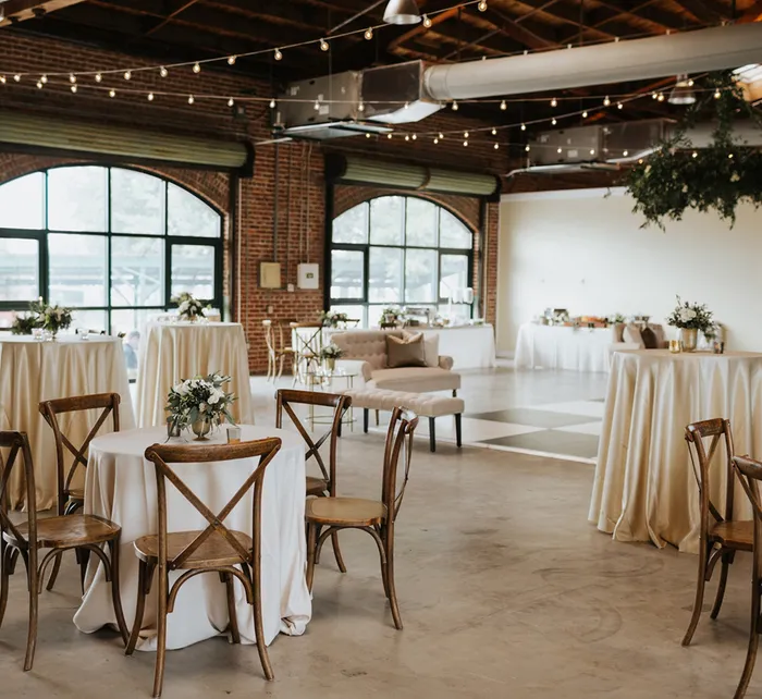 Indoor wedding venue at Morean Center for Clay with long tables, black chairs, string lights, and large arched windows