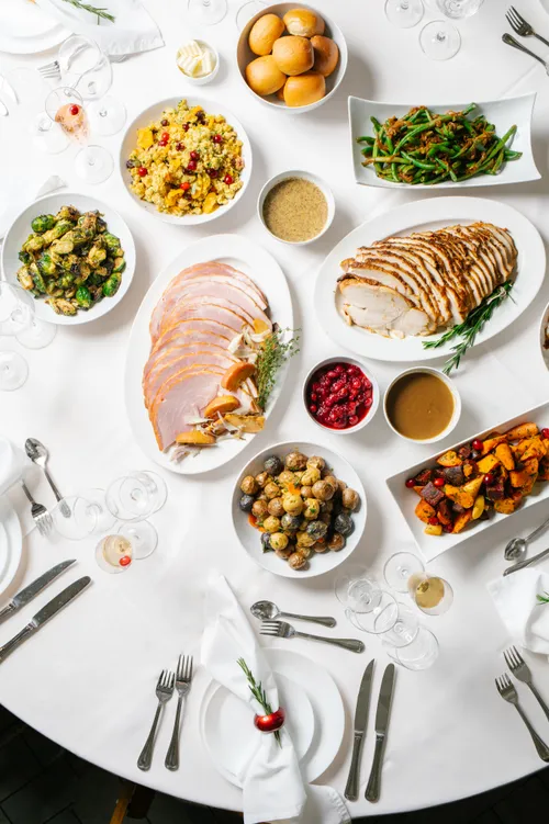 Thanksgiving catering spread with sliced turkey, ham, roasted vegetables, cranberry sauce and gravy